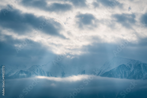 Winter mountains covered with snow between clouds with bright sunrays shining through, Mieminger Plateau, Tirol, Austria