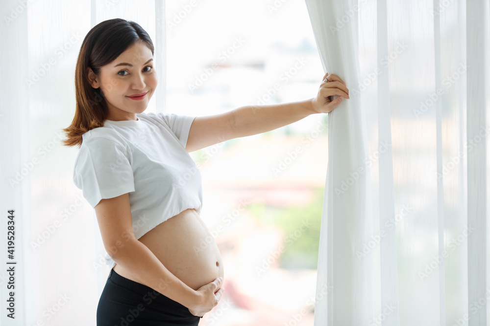 Asian woman pregnant mother standing by the window in white bedroom Asian woman pregnant mother standing by the window in white bedroom
