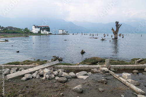 House at the coast of lake Atitlan with dead tree along misty mountains, San Pedro la Laguna, Guatemala photo