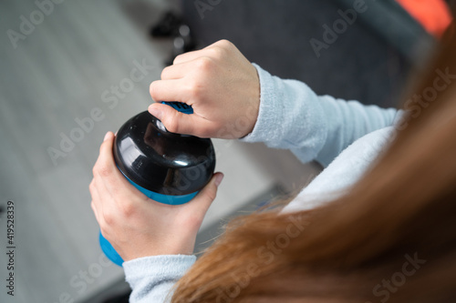 Close up on hands of unknown caucasian woman holding supplement shaker while standing in room at home opening or closing top view