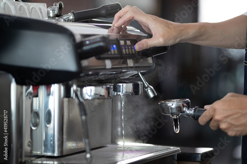 Close up of warm water rinsing at the pouring from coffee machine. A man barista preparing for pressing ground coffee for brewing espresso or americano in a cafe.