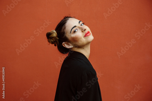 Schilderij op canvas Portrait of a spanish woman, smiling, looking at the camera, with a red wall of the street on the background