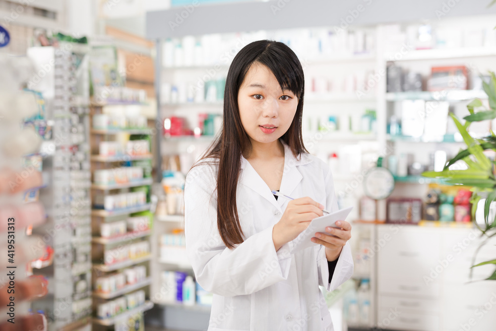 Chinese female is checking medicine with notebook in pharmacy. High quality photo