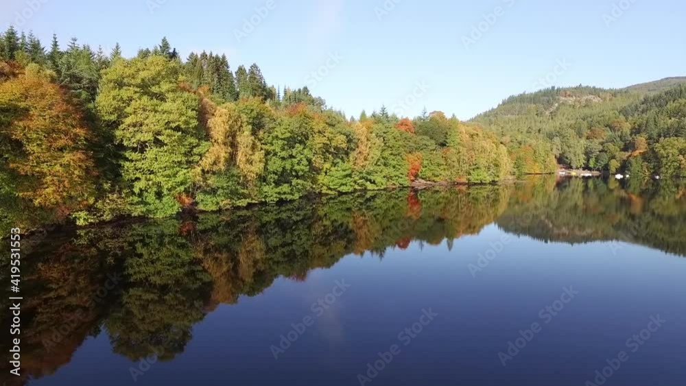Aerial Forward: Glass Still Lake Reflecting Dense Waterfront Forest With Autumn Trees In The Sunshine Aerial Forward: Glass Still Lake Reflecting Dense Waterfront Forest With Autumn Trees In The Sunshine