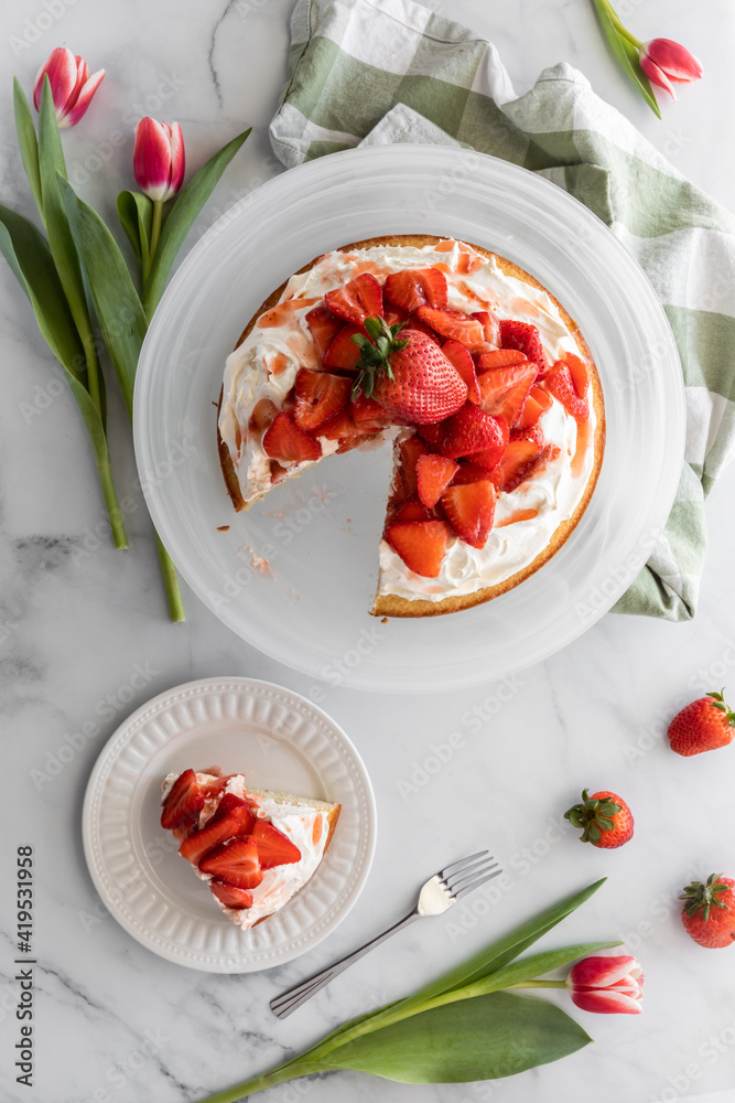 Samolepka Top down view of a strawberry shortcake with one slice served on a small plate beside and tulips surrounding