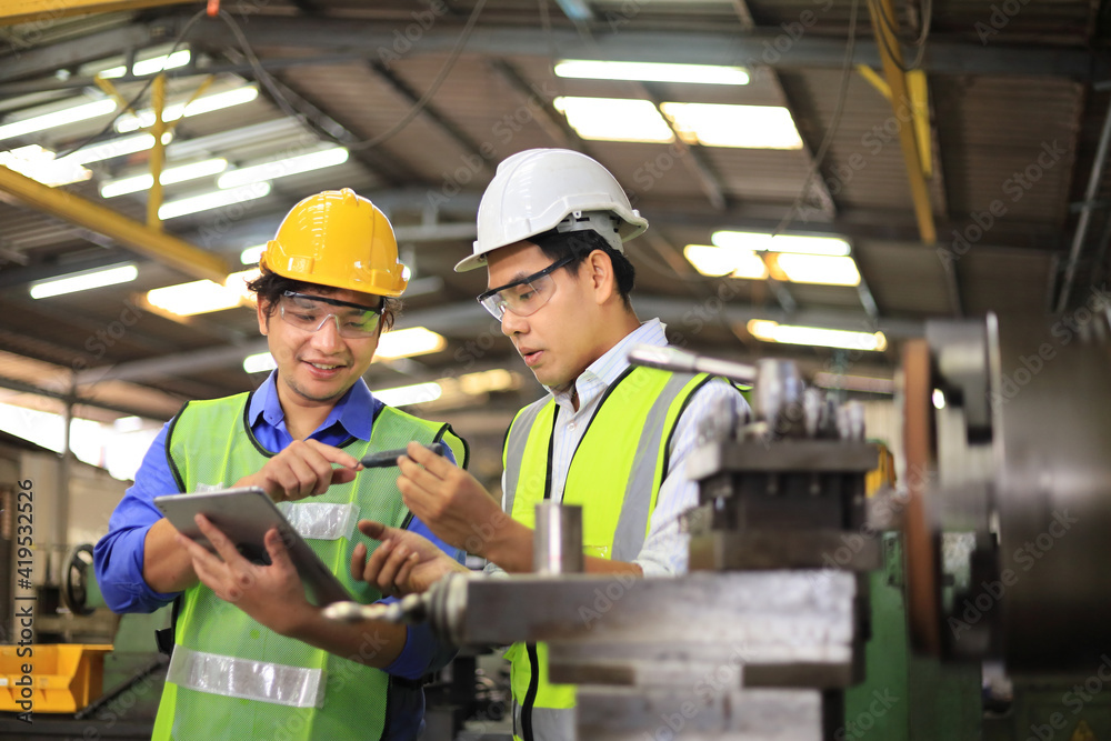 Asian engineering manager and mechanic worker in safety hard hat and reflective cloth using lathe machine inside the factory Asian engineering manager and mechanic worker in safety hard hat and reflective cloth using lathe machine inside the factory