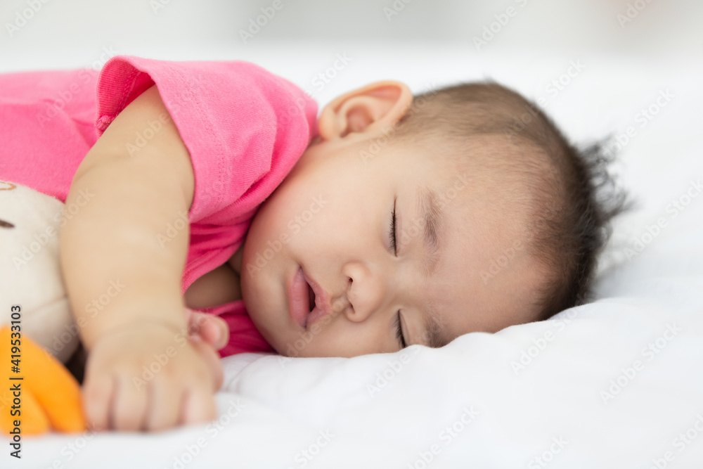 Focus close up to asian adorable baby child deep sleeping on white bed feeling comfortable and hugging doll Focus close up to asian adorable baby child deep sleeping on white bed feeling comfortable and hugging doll