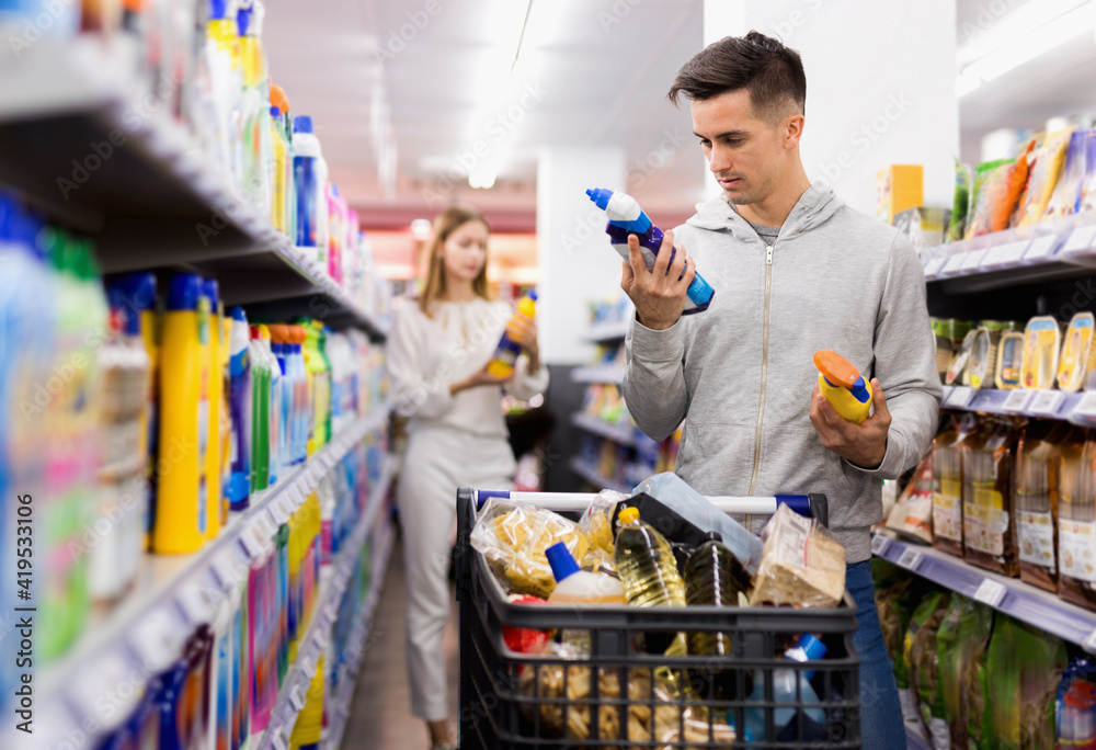 Young glad positive male customer making purchases in supermarket, buying household chemicals