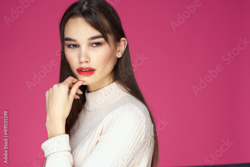 Brunette with long hair red lips cosmetics white sweater pink background cropped view