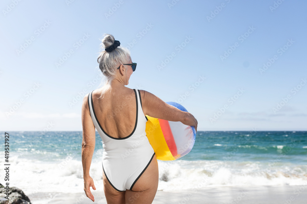 Mature woman holding a beach ball while in a swimsuit