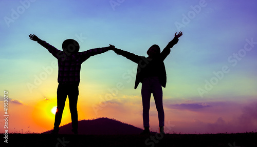 Silhouette of young couples, nature tourists stand release their freedom and enjoy the evening near the mountain with twilight sunset. Concept of relationship and Successful. Soft focus and blur