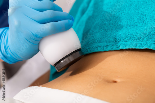 Closeup of female abdomen during professional ultrasonic fat cavitation procedure in cosmetology clinic photo