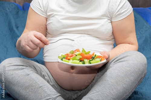 Closeup of a pregnant woman holding a plate of sliced vegetable salad. Healthy lifestyle and nutrition concept during pregnancy