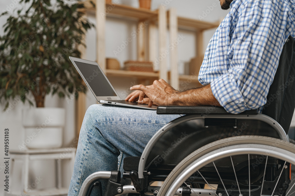 Disabled man sitting in a wheelchair and using laptop