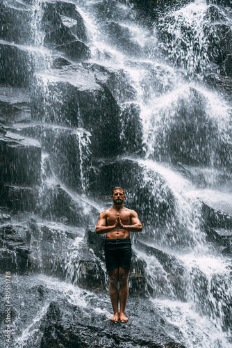 A man does yoga at a waterfall. Healthy lifestyle. The concentration of the body. A man does yoga in Bali. A man meditates in nature. Meditation at the waterfall. Young man practicing yoga. Copy space