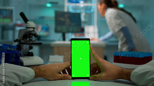 POV shot of chemist using smartphone with green screen in biological laboratory. Medical worker wearing white coat in clinic working with mobile with chroma key on isolated display in medical lab