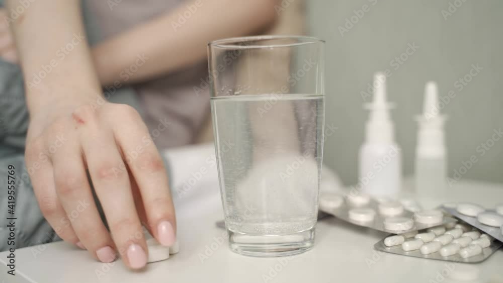 Close-up of a glass with a dissolving tablet on a bedside table. In the background a sick girl waiting in bed
