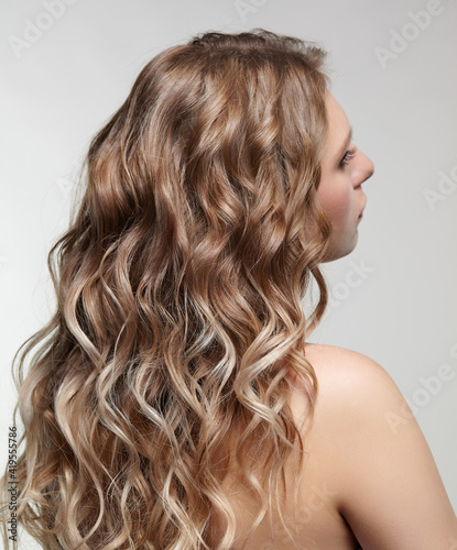 Woman from backside on gray background. Female with curly hair