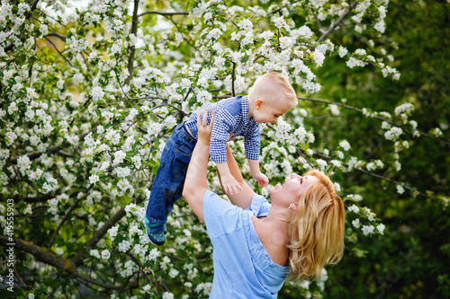 Mom and son in a blooming apple orchard in spring. A woman holds a child in her arms, plays and has fun with it.