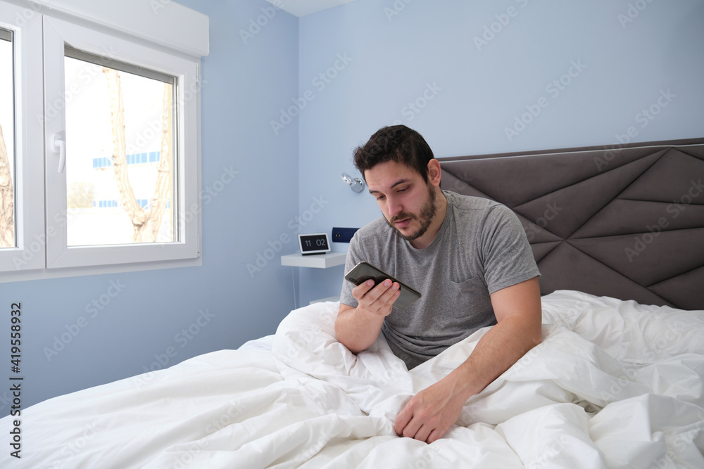 Young latin man tired in bed after sleeping and checking his smartphone. Late in the morning. Young latin man tired in bed after sleeping and checking his smartphone. Late in the morning.