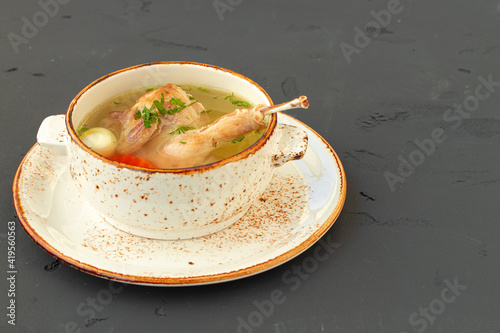 Chicken broth with chicken half in white bowl on gray background