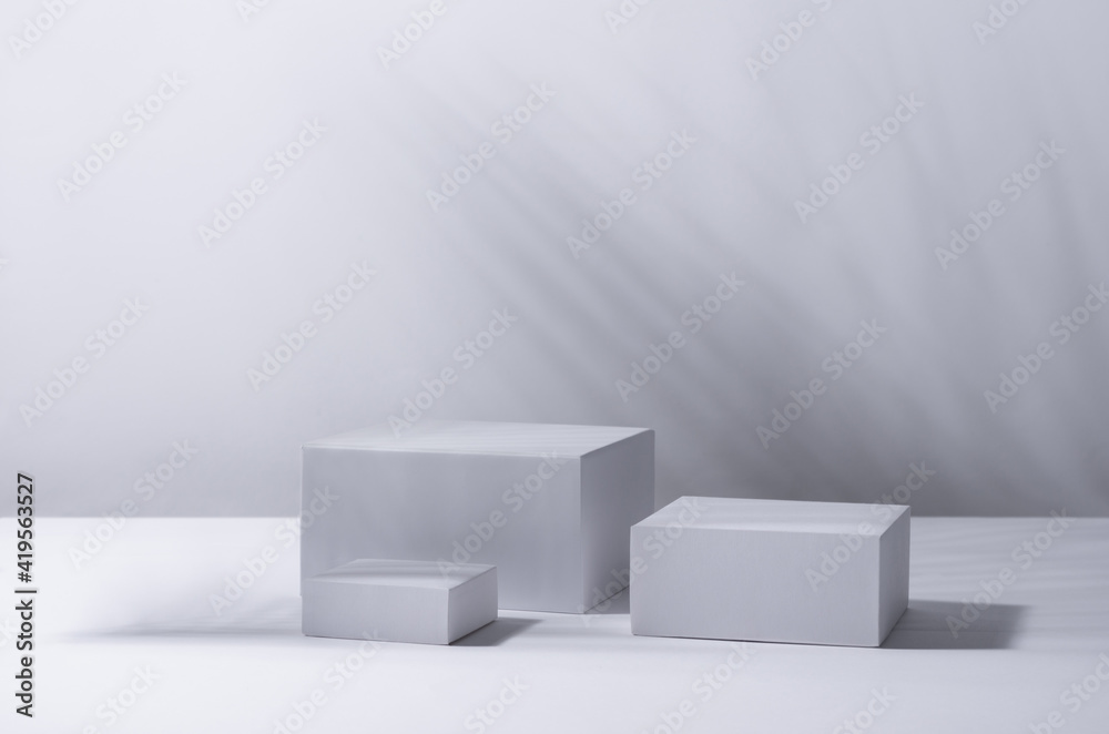 White square podiums in sunlight with shadow palm leaf in white space. Tropical showcase for cosmetic products, goods, shoes, bags, watches. White square podiums in sunlight with shadow palm leaf in white space. Tropical showcase for cosmetic products, goods, shoes, bags, watches.