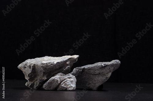 Rough natural grey stone as podium for packaging and cosmetic presentation on black background, copy space.