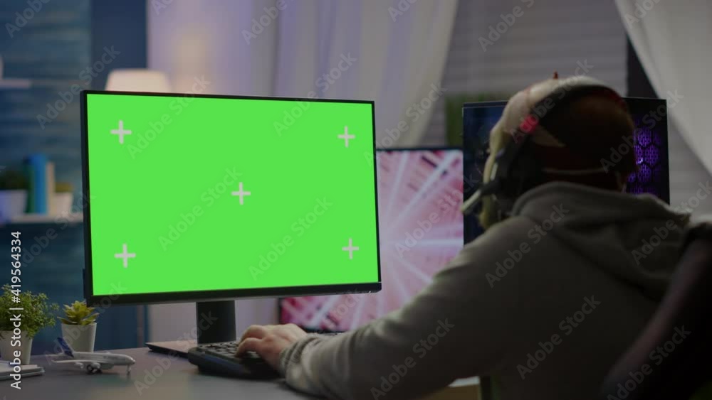 Professional cyber gamer playing video games with greenscreen, chroma key, mock up desktop isolated display. Player using powerful computer with mockup screen streaming shooter games wearing headset Professional cyber gamer playing video games with greenscreen, chroma key, mock up desktop isolated display. Player using powerful computer with mockup screen streaming shooter games wearing headset