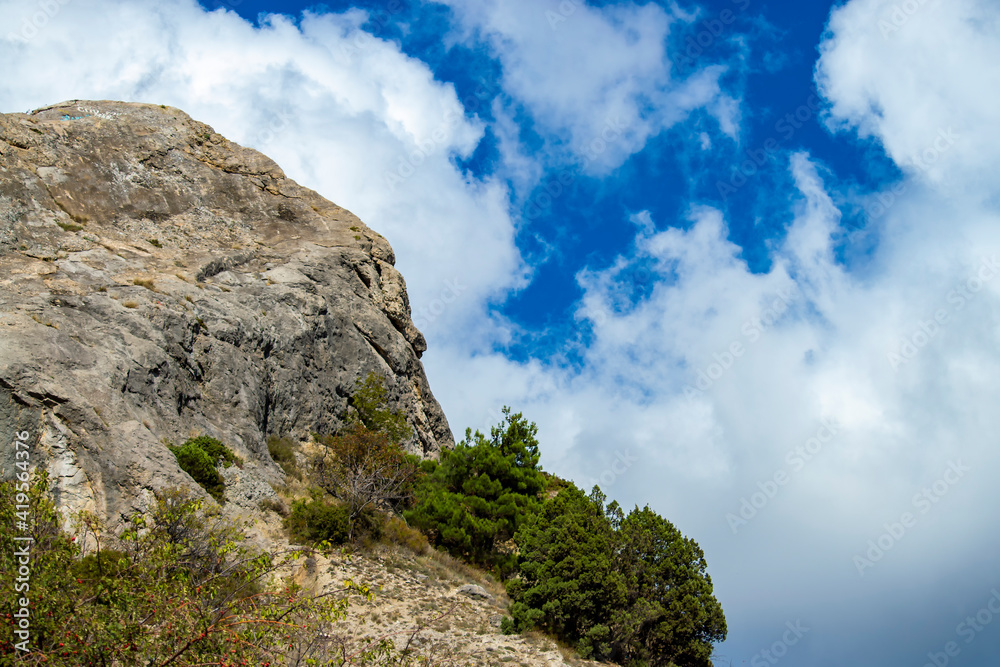 Rock and vegetation are scarce in Crimea against clouds and sky.