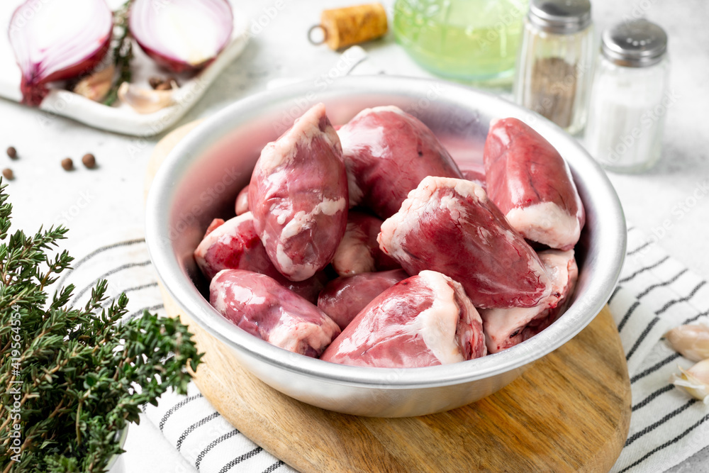 Turkey hearts. Raw turkey hearts in a metal bowl on a light gray table Turkey hearts. Raw turkey hearts in a metal bowl on a light gray table