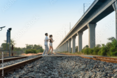 Blured defocused Young active Asian couple in sportswear jogging together across the empty railway tracks filled with small rocks and crushed stones with long highway bridge clear blue sky background