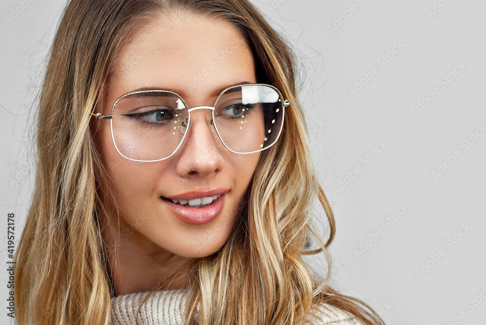 Girl in a sweater on a white wall background. Woman in glasses with a gold frame.