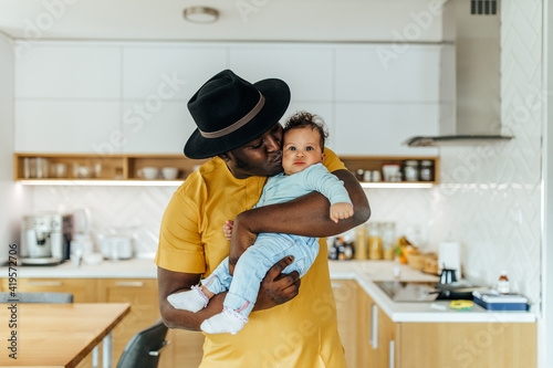  African man wearing black hat and yellow suit, holding baby.
