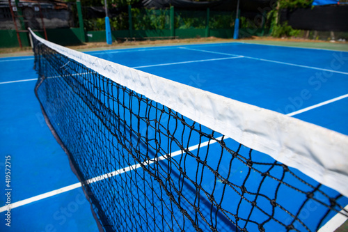 Blue tennis court with net in park. Empty sport field photo. Hard cover for lawn tennis. Summer sport activity outdoor. White markup on blue court. Sunny day on tennis court. Sport field in park