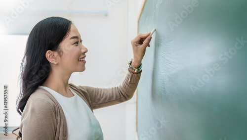 Closeup portrait of young happy asian teacher write on chalk board. student writing on blackboard wall. Idea creative education spelling teaching knowledge back to school concept