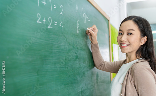 Closeup portrait of young happy asian teacher write on chalk board. Woman writing on blackboard wall. Idea creative education teaching math and spelling letter, knowledge, back to school concept