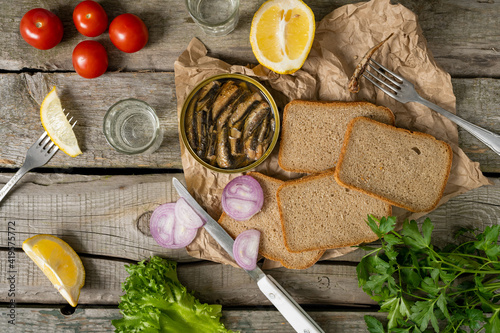 Sandwich with smoked sprats in oil with tomatoes, lemon, herbs and vodka on wooden table