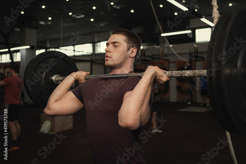 Handsome muscular male athlete doing shoulder press with barbell at gym