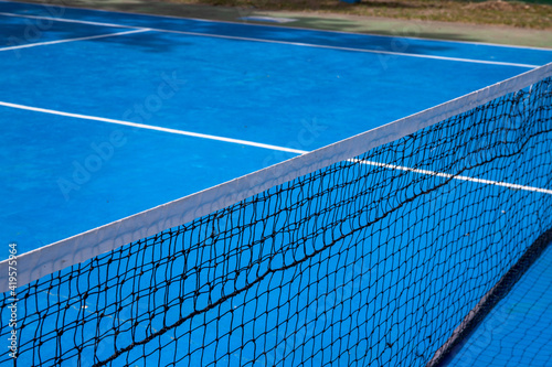 Sunny blue tennis court with net. Empty sport field photo. Hard court cover for lawn tennis. Summer sport activity outdoor. White markup on blue court. Sunny day on tennis court. Sport field in park