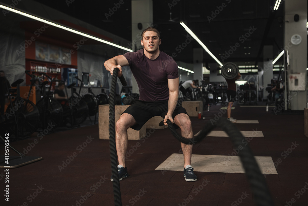 Strong male athlete exercising with battle ropes at the gym, copy space