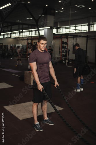 Vertical shot of a handsome muscular athletic man resting after exercising with battle ropes at gym