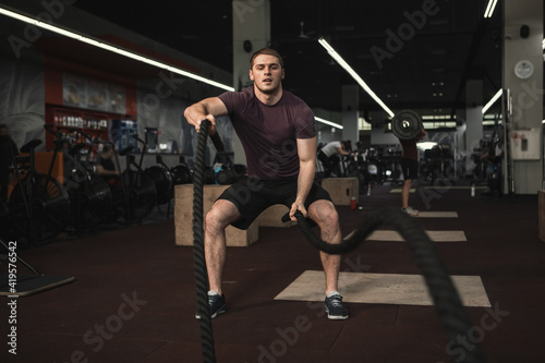 Strong male athlete exercising with battle ropes at the gym  copy space