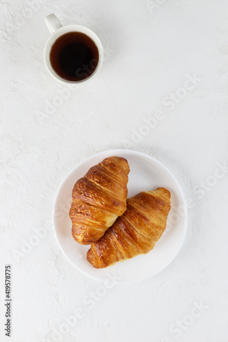 Fresh croissants on a white plate with a cup of coffee. Vertical orientation, top view.