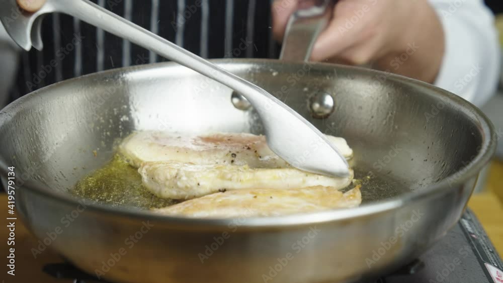 Chef fries chicken breast in metal frying pan. Slow motion shot Chef fries chicken breast in metal frying pan. Slow motion shot