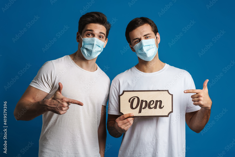 Joyful guys in protective masks gesturing while showing open sign board
