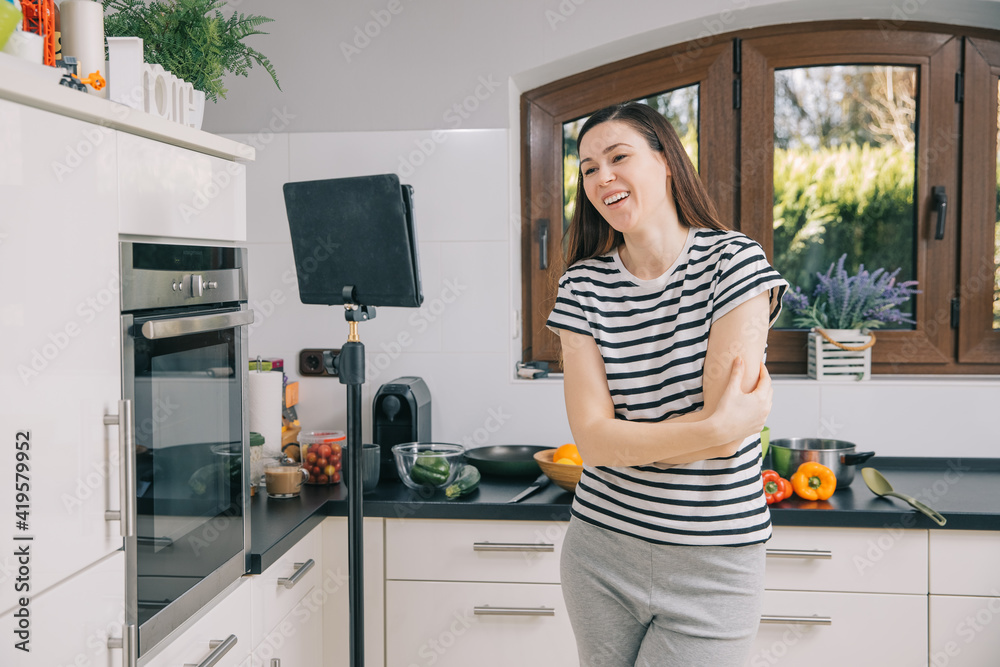 Young woman shows online how to prepare healthy and tasty food at home. Blogger takes a video in her kitchen. Online healthy eating courses. Video blog from home during the pandemic. 