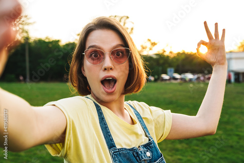 Image of surprised brunette woman taking selfie and showing ok sign