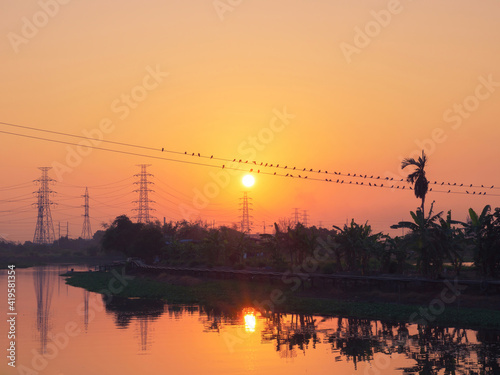 silhouette scenic of twilight sky with  electricity transmission tower and reflection on water with  birds on power line at waterfront in morning sunsine photo