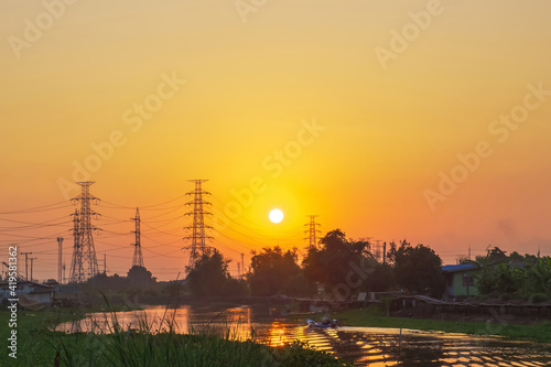 silhouette scenic of beautiful sunrise sky with  electricity transmission tower and reflection on water wave surface of countryside house with fisherman boat a traditional waterfront lifestyle