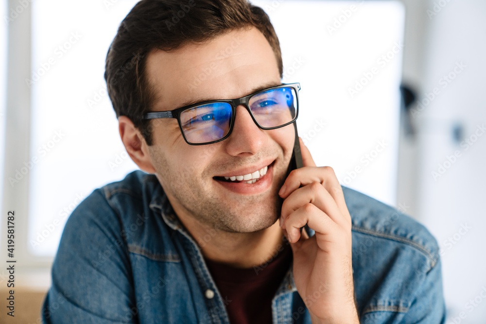 Happy handsome man in eyeglasses smiling and talking on mobile phone